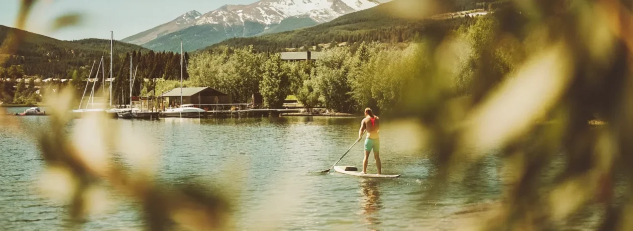 Stand-up paddleboarder on turquoise Lake Dillon with snow-capped mountains and Dillon Marina docks in background