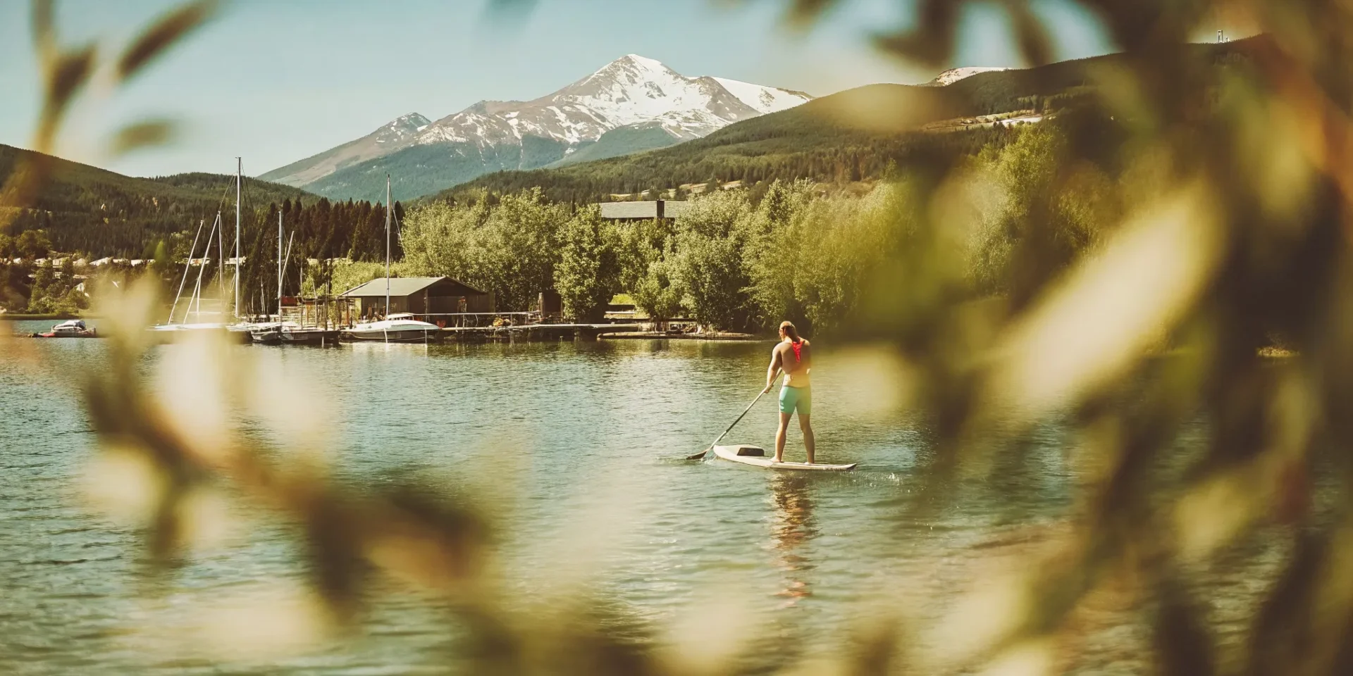 Stand-up paddleboarder on turquoise Lake Dillon with snow-capped mountains and Dillon Marina docks in background