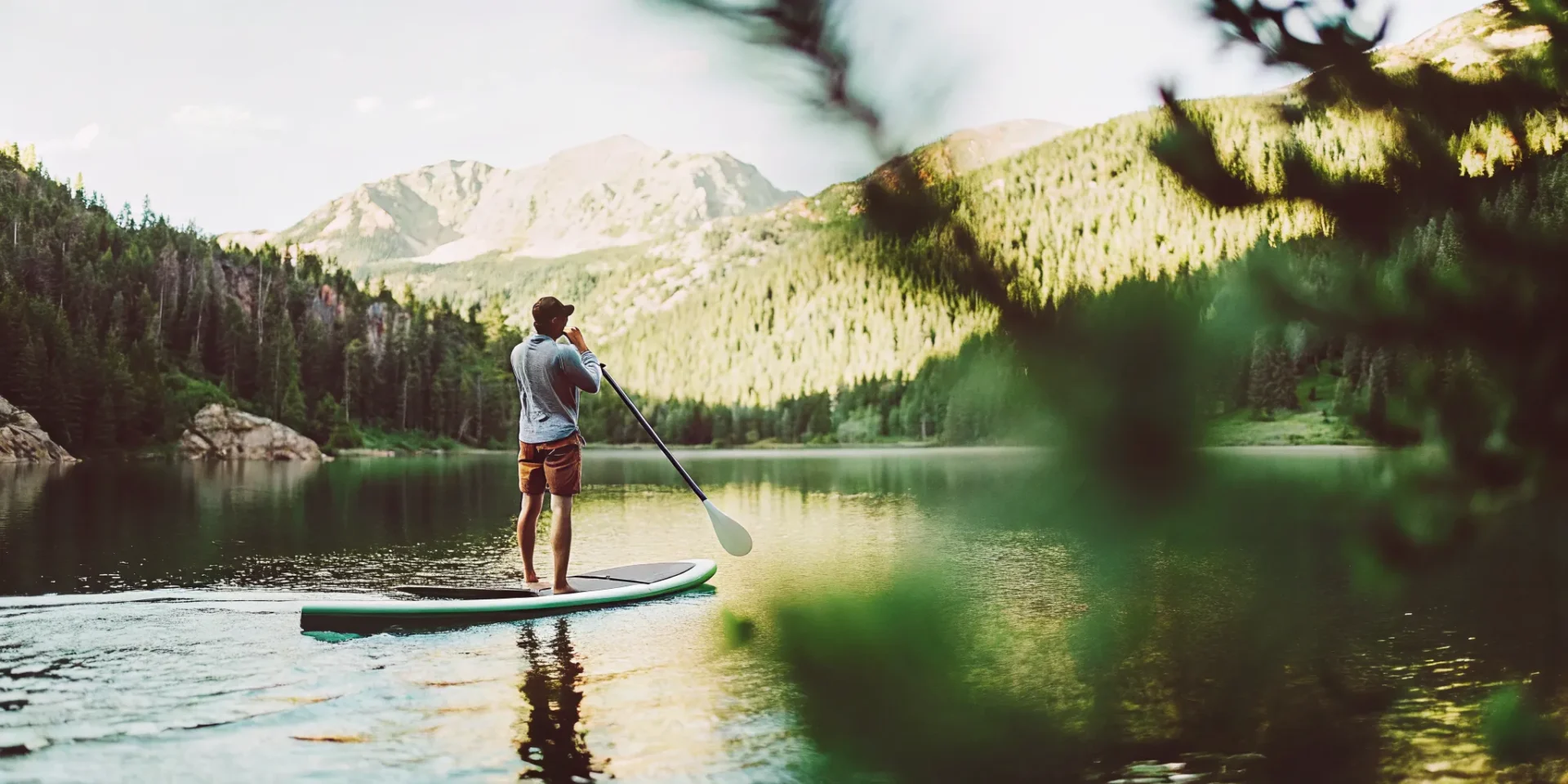Person stand-up paddle boarding on a calm mountain lake in Colorado with Rocky Mountain peaks in the background
